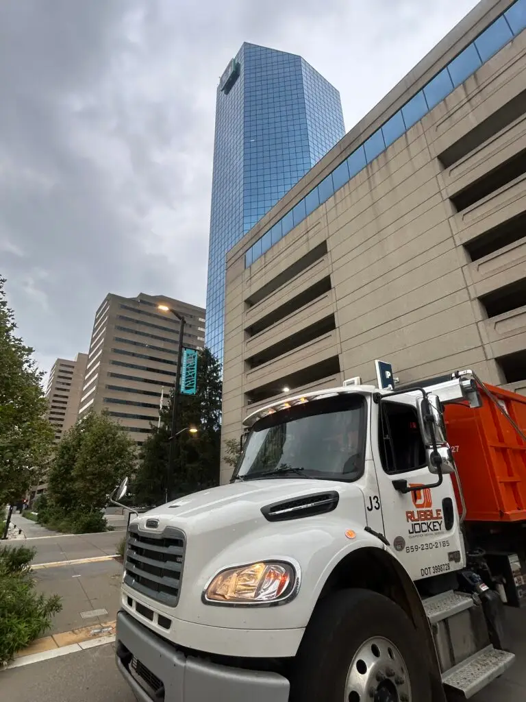 Rubble Jockey&rsquo;s white J3 hook-lift truck carrying an orange dumpster beside the Fifth Third building in downtown Lexington.